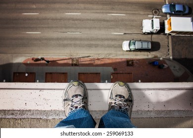 Man Standing On Edge Of Tall Building Looking Down Upon The Road With Moving Cars Passing By Below (shallow Depth Of Field)