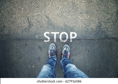 Man Standing On Grunge Asphalt City Street With Written Stop Sign On The Floor, Point Of View Perspective.