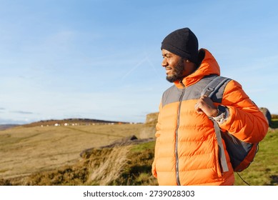 Man standing on hillside with backpack during clear day in the countryside