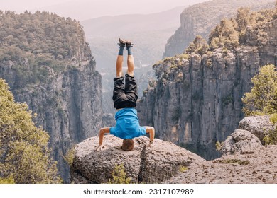 Man standing on his head on the edge of a big cliff with view of canyon Tazi in Turkey. Yoga pose concept