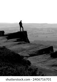 A man standing on the jagged edge of the cliff overlooking the landscape, and studying a map.  Curbar Edge, Peak District, Derbyshire, UK.  Countryside navigation; planning his route.  September 2009.