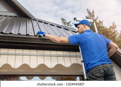 Man Standing On Ladder And Cleaning Roof Rain Gutter From Dirt