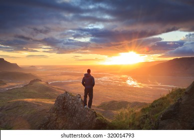 Man standing on a ledge of a mountain, enjoying the beautiful sunset over a wide river valley in Thorsmork, Iceland. - Powered by Shutterstock