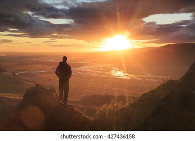 Man standing on a ledge of a mountain, enjoying the sunset over a river valley in Thorsmork, Iceland. With lens flare. 