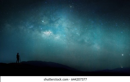 The man standing on the mountain cliff at night looking full stars on sky with beautiful light of milky way galaxy. panorama shot