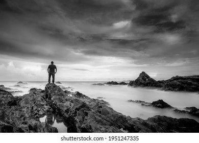 Man Standing On A Rocky Coastline, A Slow Shutter Speed Was Used To See The Movement . Soft And Grain Image.