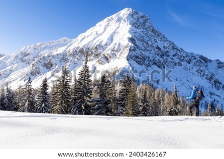 Man standing on snow field with scenic view on snow capped mountain peak of Mittagskogel (Kepa) in Karawanks, Carinthia, Austria. Winter wonderland in Austrian Alps. Snowshoe hiking snowy landscape