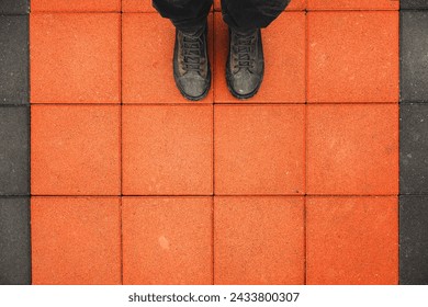 Man standing on the square shaped concrete pavement slabs, top view of dirty boots on orange sidewalk with copy space - Powered by Shutterstock