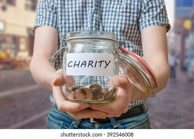 Man Standing On Street Is Collecting Money For Charity And Holds Jar With Coins.