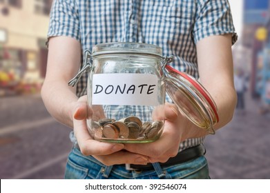 Man Standing On Street Is Collecting Donations In Jar.