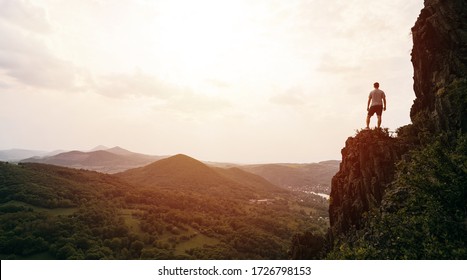 Человек, стоящий на вершине горы на закате. Фотокомпозит концепции целей и достижений. Концептуальное видение, путешественник смотрит на гору и наслаждается восходом солнца