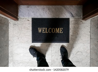 A man standing on top of a welcome floor mat in front of an apartment door