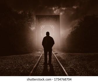 Man Standing On Train Tracks Silhouetted By The Light Of An On Coming Train At Night Contemplating Suicide.