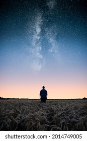 Man Standing On Wheat Field Under The Stars Of The Milky Way At Night. Man Looking At Stars And Dreaming.