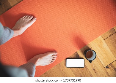 Man Standing On Yoga Mat With Coffee And Mobile Phone Shot From Above.