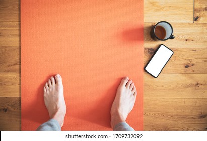 Man Standing On Yoga Mat With Coffee And Mobile Phone Shot From Above.