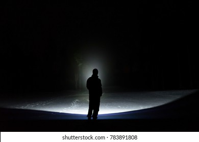 Man standing outdoor at night in forest shining forward with flashlight. Nice strong light beam. Beautiful abstract photo. Calm, peaceful and mystical image.