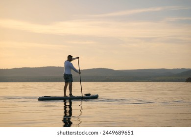  A man is standing and paddling on a paddleboard on the water at sunset. Enjoying life.  - Powered by Shutterstock