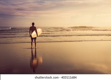 A man is standing with a surf in his hands on the sea shore.  - Shutterstock ID 403111684
