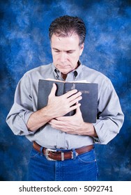 A Man Standing And Tenderly Holding An Old Bible To His Chest.