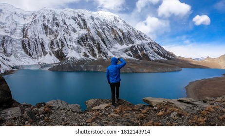 Man standing at the turquoise colored Tilicho lake in Himalayas, Manang region in Nepal. The world's highest altitude lake (4949m). Snow capped mountains around. Calm surface of the lake. Achievement