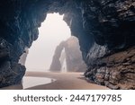 Man standing under natural arch on Cathedrals beach in Galicia, Spainn. Tourist silhouette in foggy landscape with Playa de Las Catedrales Catedrais beach in Ribadeo, Lugo on Cantabrian coast