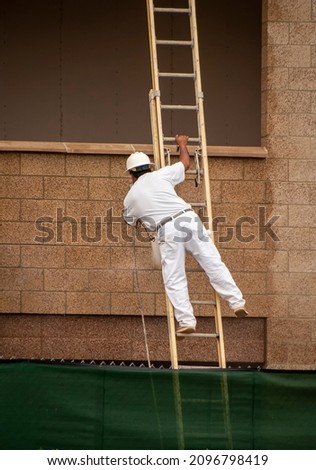 Man standing unsafely on a ladder power washing a wall dressed in white 