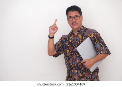 Man standing wearing Batik shirt and holding laptop in left hand