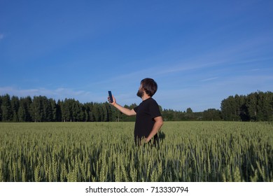 Man Standing In The Wheat, Rye Field Holding His Mobile Phone In Search Of Mobile Reception, Looking On His Cell Phone.