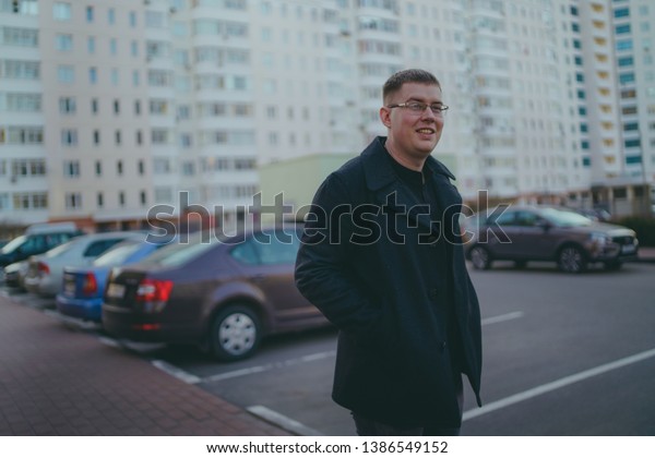 Man\
standing in yard of city\
Portrait of young man in casual clothes\
standing beside cars in yard of high-rise\
buildings