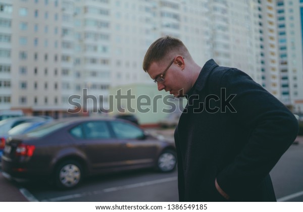 Man\
standing in yard of city\
Portrait of young man in casual clothes\
standing beside cars in yard of high-rise\
buildings