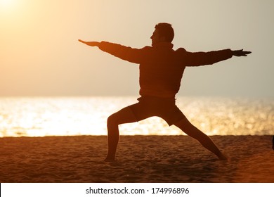 Man standing in yoga warrior pose on ocean beach.