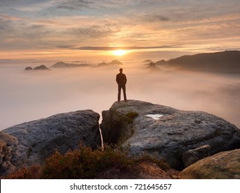 Man Stands Alone On The Peak Of Rock. Hiker Watching To Autumn  Sun At Horizon . Beautiful Moment The Miracle Of Nature. Colorful Mist In Valley. Man Hike. Person Silhouette Stand