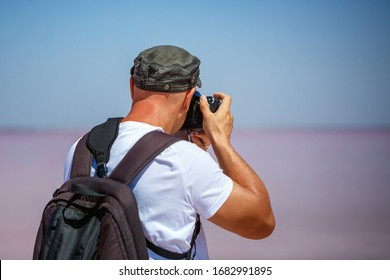 A man stands back with a backpack taking photos of nature, salty pink lake.