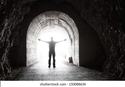 Man stands in dark tunnel with glowing end