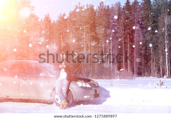 a man\
stands in front of a broken car in the\
winter