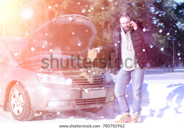 a man\
stands in front of a broken car in the\
winter