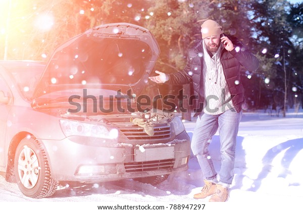 a man
stands in front of a broken car in the
winter