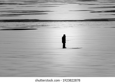 A Man Stands In Front Of His Ice Fishing Hole On Lake McDonald, Glacier National Park Waiting For A Fish To Bite.