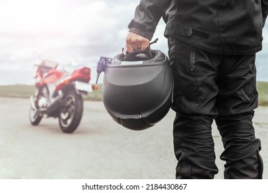A man stands with his back to his motorcycle, holding a helmet