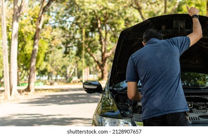 Man stands and inspects a broken-down car in a rural suburban forest. Black car, Engine won't start. Concept for roadside, damaged, stress, fix, problem. Close up, Selective focus, blurred background