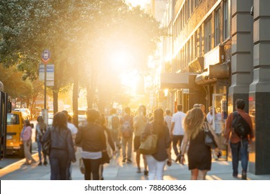 Man Stands In The Middle Of A Busy Sidewalk Looking At His Cell Phone While Crowds Of People Walk Around On 14th Street In Manhattan, New York City With The Glow Of Sunlight In The Background.