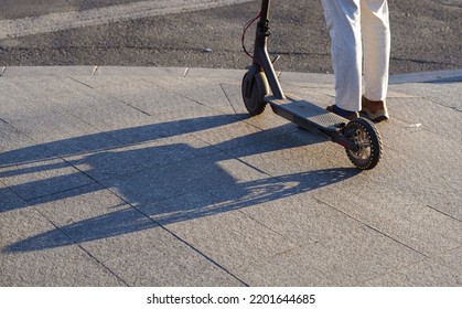 A man stands next to his electrical scooter at a pedestrian crosswalk. Eco way to comute in the crowded cities. Concept photo for e-scooter transportation