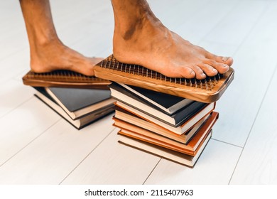 A man stands on a board with nails. The sadhu board is on the stack of books. The concept of spiritual growth and development of emotional intelligence. Wooden sadhu board with nails for sadhu practi