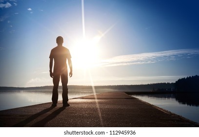 A man stands on the concrete pier starring at the setting Sun