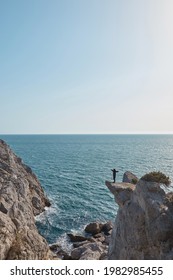 a man stands on the edge of a cliff, hands spread out in different directions, seascape and mountains