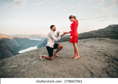 A man stands on his knee near the cliff and makes a creative proposal to a woman traveling in trolltunga, Norway. Emotional couple in love, engagement, rocks, nature, fjords. She said yes on the top.