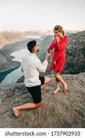 A man stands on his knees near the cliff and makes a creative proposal to a woman traveling in trolltunga, Norway. Emotional couple in love, engagement, rocks, nature, fjords. She said yes on the top.