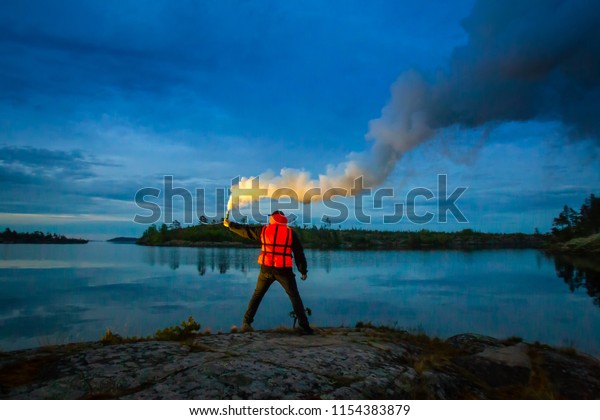 A man stands on an island with a\
torch in his hand. Smoke bomb. A signal for help. The man in the\
rescue jelly. At night, a man signals a smoke\
sword.