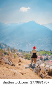 A man stands on a mountain path overlooking a valley and mountains in Tungnath Temple, Chopta, Uttarakhand, India. The scenic view showcases the beauty of nature and the tranquility of the surroundings.